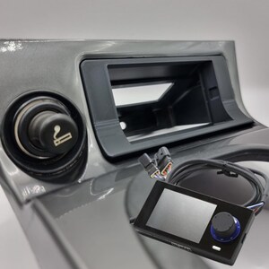 May include: A black and gray car dashboard with a cigarette lighter, a blank rectangular space, and a black and blue device with a knob and a screen.