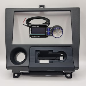 May include: A black plastic car radio dash kit with a Pro-Fec controller and a knob. The controller has a small LCD screen and a blue knob.
