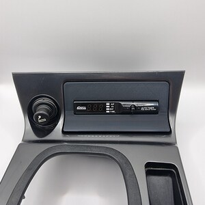May include: A black plastic car center console with a cigarette lighter, a digital clock display showing 8.8.8, and a button labeled "AUTO TIMER for NA & Turbo".