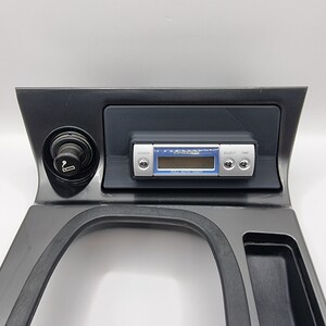 May include: A black plastic car dashboard with a cigarette lighter, a black storage compartment, and a silver digital clock radio with the text "PIAA Auto Timer".