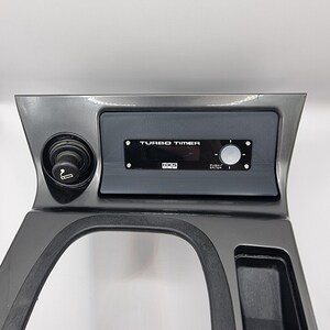May include: A black car interior panel with a cigarette lighter, a turbo timer with a digital display, and a knob labeled "Push Enter".