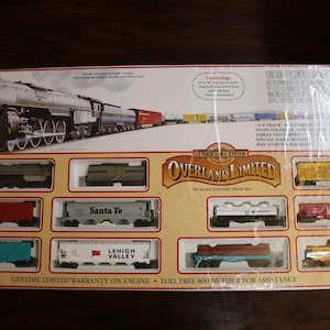 May include: A boxed Overland Limited HO scale electric train set featuring a steam locomotive with tender and various freight cars. The packaging displays the train, track system details, and includes a lifetime warranty on the engine.