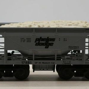 May include: A gray model train car with the words "Phelps Dodge" printed on the side. The car is loaded with white sand and has the number "17881" printed on the side. The car is a Lionel O Gauge Museum Car.