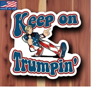 May include: A sticker with the text "Keep on Trumpin'" in blue and white, featuring a cartoon figure in a suit with an American flag design. The sticker has a white border and a small American flag in the upper left corner.