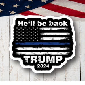 May include: A white sticker with a blue line American flag and the text "He'll be back TRUMP 2024".