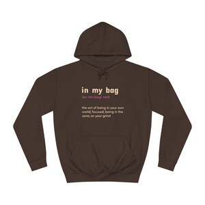 May include: A brown hoodie with a front pocket and a hood. The text "in my bag" is printed on the front, along with a definition. The hoodie is made of a soft material and is suitable for casual wear.