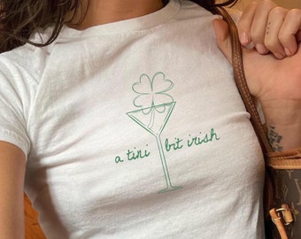 May include: White t-shirt with a green four-leaf clover in a martini glass design. The text "a tiny bit irish" is printed below the glass.