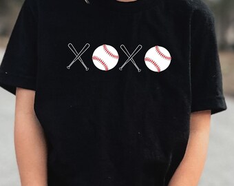 Op de afbeelding: Zwart T-shirt met een witte afbeelding van twee honkballen en twee gekruiste knuppels. De afbeelding luidt "XOXO".