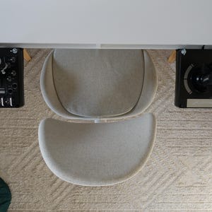Peut inclure: Vue aérienne d'un espace de travail moderne avec un bureau blanc et deux panneaux de contrôle noirs. Une chaise grise et incurvée est devant le bureau. L'ensemble est posé sur un tapis beige à motifs.