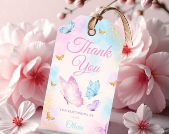 May include: A pastel-colored gift tag with the words "Thank You" in script. The tag features watercolor butterflies in shades of pink, blue, and purple, with gold accents. The tag is tied with a natural twine and is surrounded by pink flowers.