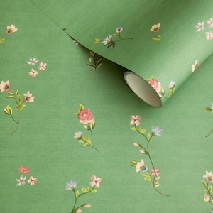 Könnte beinhalten: Grüne Blumentapete mit einem sich wiederholenden Muster aus rosa, blauen und weißen Blumen. Die Tapete ist ausgerollt und zeigt eine Rolle mit dem gleichen Design. Das Design hat eine weiche, botanische Ästhetik.