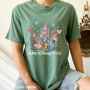 May include: A light green t-shirt featuring a colorful graphic of Disney characters, including Woody, Buzz Lightyear, and Jessie, in front of a castle. The text "Walt Disney World" is printed below the characters. The shirt also has the text "LIGH GREEN" at the bottom.