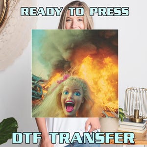 May include: A DTF transfer featuring a doll's face with wide blue eyes and an open mouth, set against a backdrop of flames and a car. The text "READY TO PRESS" and "DTF TRANSFER" are displayed in a light blue font.