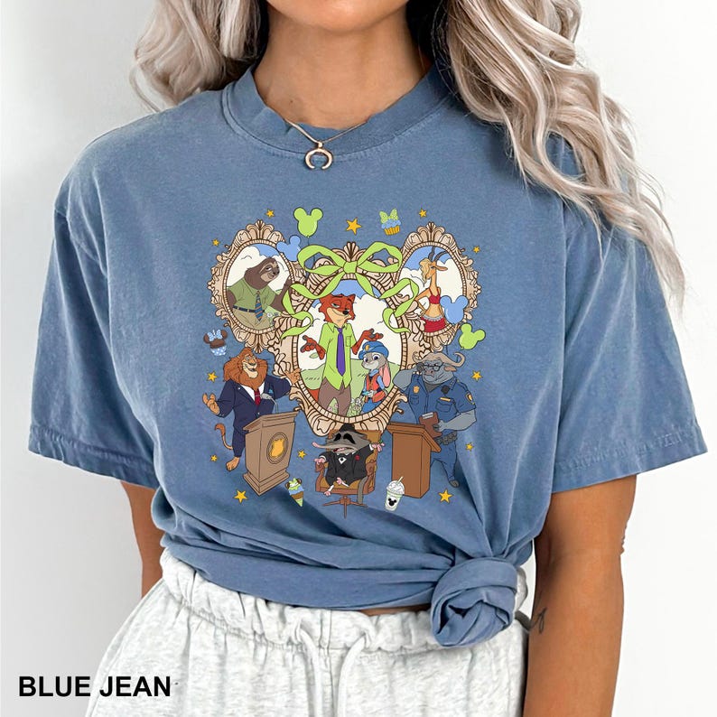 May include: Blue jean colored t-shirt featuring a cartoon graphic of characters in ornate frames. The graphic includes a fox, bunny, lion, and other animal characters. The text "BLUE JEAN" is at the bottom of the shirt.