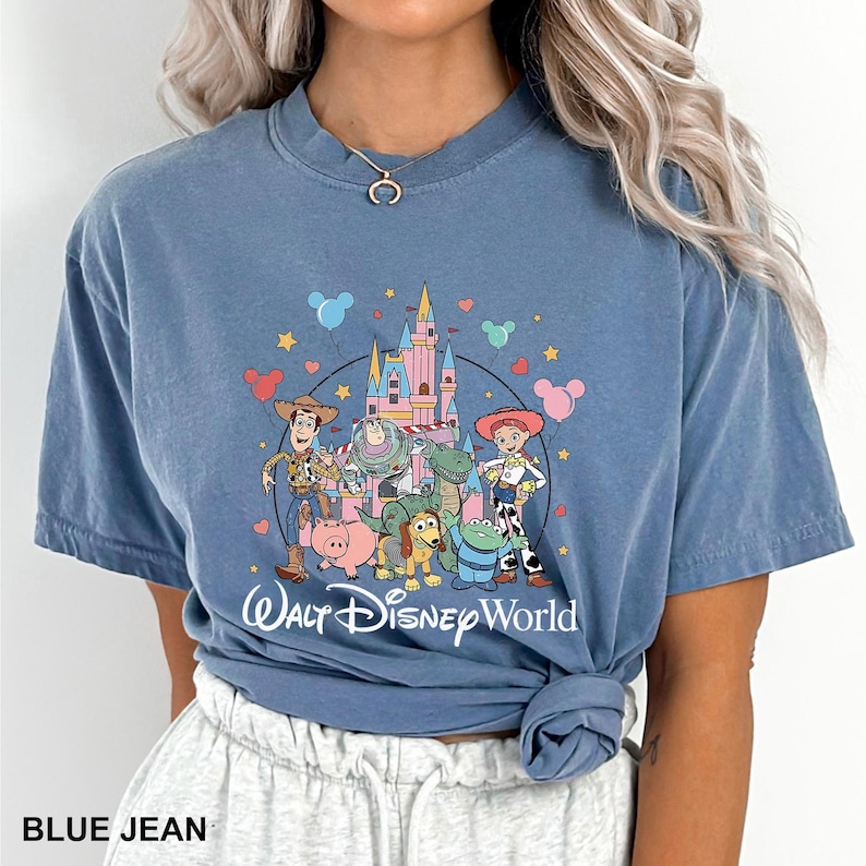 May include: A blue jean colored t-shirt featuring a colorful graphic of Disney characters and a castle. The words "Walt Disney World" are printed below the graphic. The shirt has short sleeves and a crew neck.