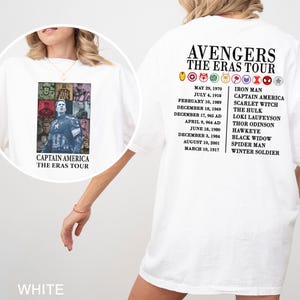 May include: White t-shirt featuring a Captain America graphic on the front and "Avengers The Eras Tour" text on the back. The back also lists character names and dates. The shirt is a casual style.