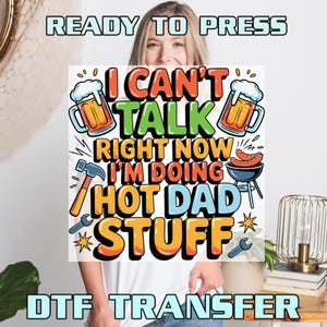 May include: A DTF transfer featuring the text I CAN'T TALK RIGHT NOW I'M DOING HOT DAD STUFF in bold orange, green, and blue letters. The design includes illustrations of two beer mugs, a hammer, a wrench, and a grill with two sausages.
