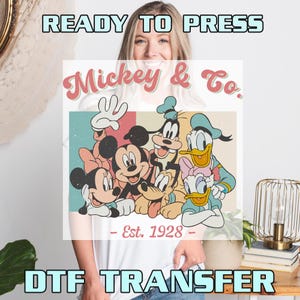 May include: Ready to press iron-on transfer featuring Mickey Mouse and friends in a retro style design. The design includes Mickey Mouse, Minnie Mouse, Donald Duck, Goofy, and Pluto. The text reads "Mickey & Co. - Est. 1928 - "