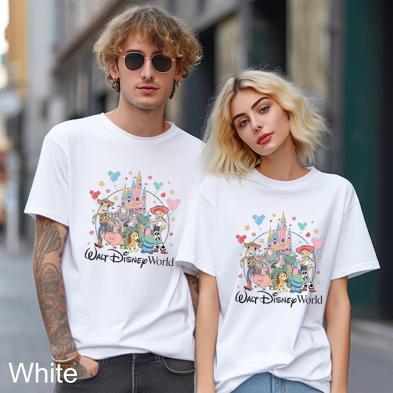 May include: White t-shirts featuring a colorful graphic of Disney characters and a castle, with the text "Walt Disney World". The shirts are worn by two people.