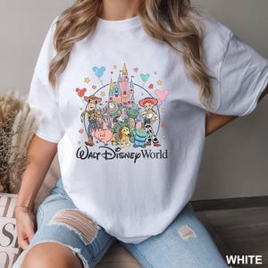 May include: White crew neck t-shirt featuring a colorful graphic of Disney's Toy Story characters and a castle, with the text "Walt Disney World" in black script. The design includes Woody, Buzz Lightyear, and other characters.