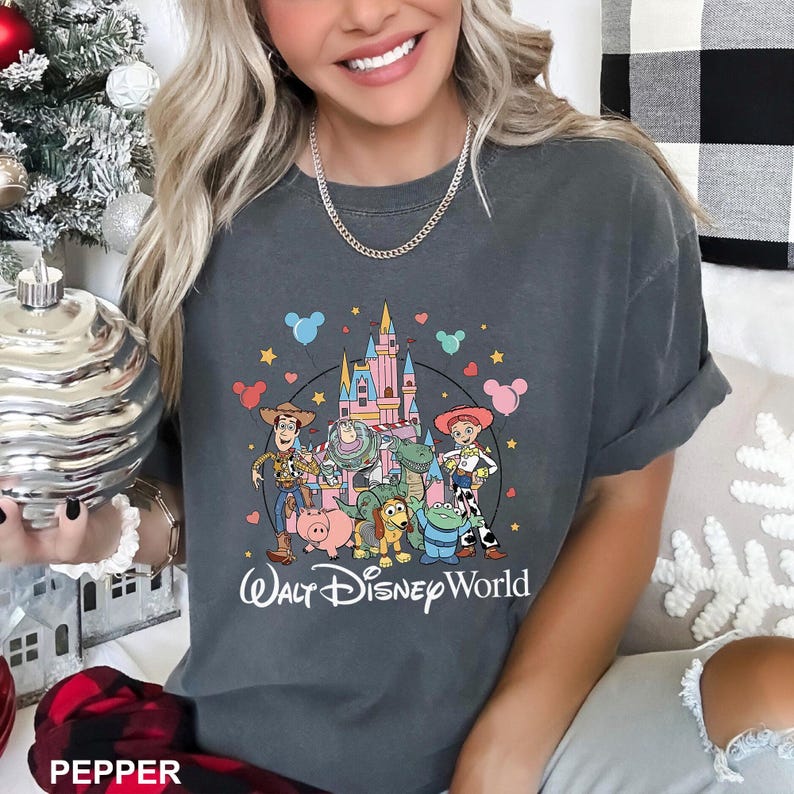 May include: Dark gray t-shirt featuring a colorful graphic of Disney characters, including Woody, Buzz Lightyear, and others, in front of a castle. The words "Walt Disney World" are printed below the graphic.