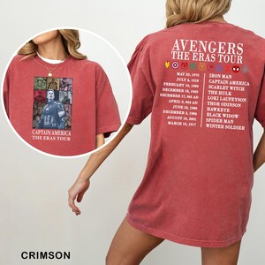 May include: Crimson-colored t-shirt featuring Captain America and the text "The Eras Tour" on the front. The back of the shirt lists Avengers characters and dates. The shirt is a comfortable, casual style.