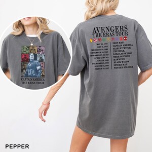 May include: Dark gray t-shirt featuring a Captain America graphic on the front and "Avengers The Eras Tour" text on the back. The shirt lists dates and character names. The shirt is a relaxed fit.