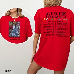 May include: Red t-shirt featuring Captain America and the text "The Eras Tour" on the front. The back of the shirt displays the Avengers logo and a list of characters and dates. The shirt is made of a soft material.