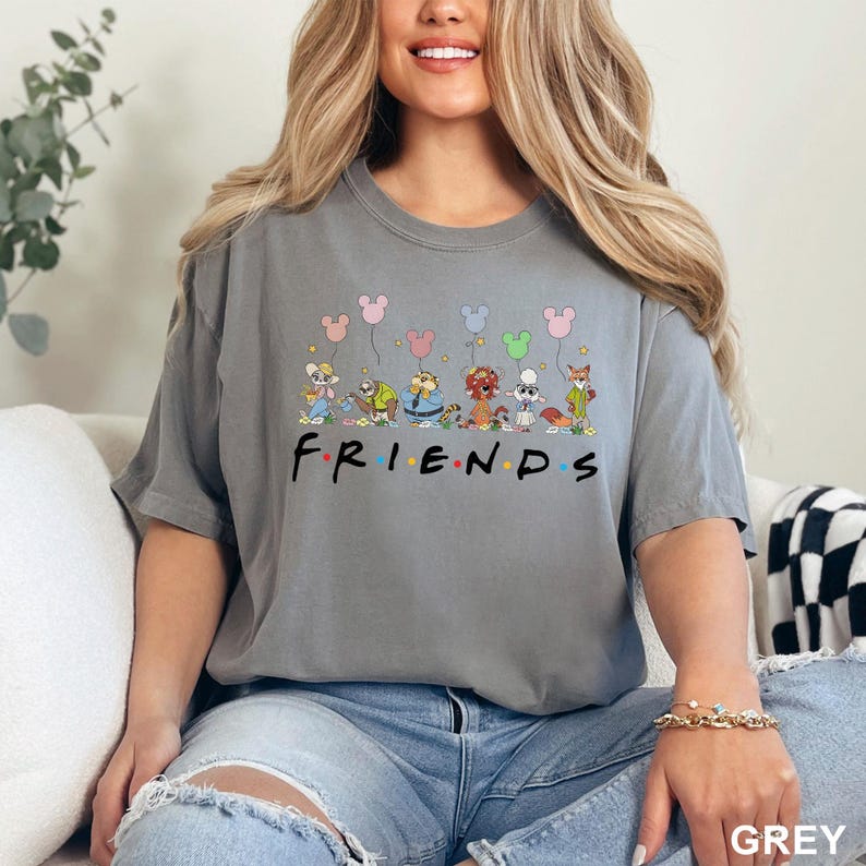May include: A grey t-shirt featuring the word "FRIENDS" in a black font. Above the word are cartoon characters holding Mickey Mouse balloons. The shirt is a solid grey color.