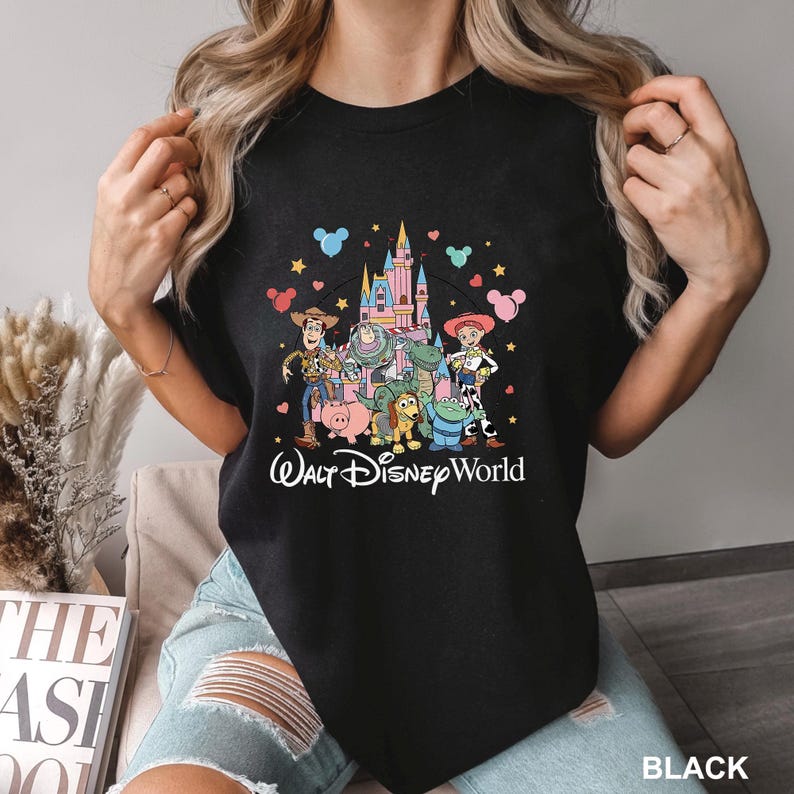 May include: Black t-shirt featuring a colorful graphic of Toy Story characters in front of a castle, with the text "Walt Disney World" in a script font. The design includes Woody, Buzz Lightyear, and other characters.
