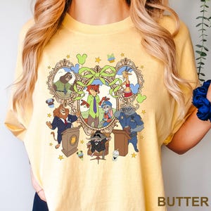 May include: Yellow t-shirt with a cartoon graphic featuring characters from Zootopia. The design includes Nick Wilde, Judy Hopps, and other characters in a decorative frame. The word "BUTTER" is printed at the bottom.