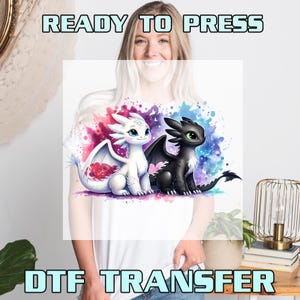 May include: White t-shirt featuring a DTF transfer design with two cartoon dragons. One dragon is white with red accents, the other is black. The words "READY TO PRESS" and "DTF TRANSFER" are printed above and below the design.