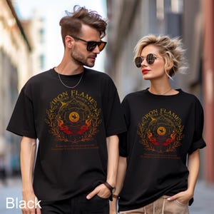 May include: Two black short-sleeved t-shirts featuring a circular graphic design with the text "IRON FLAME BURN IT DOWN". The design includes a central sun icon, stylised flames, and leafy branches in shades of orange, red, and yellow.