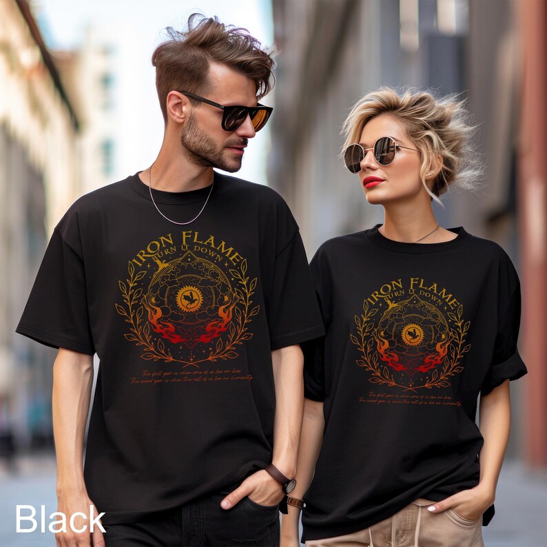 May include: Two black short-sleeved t-shirts featuring a circular graphic design with the text "IRON FLAME BURN IT DOWN". The design includes a central sun icon, stylised flames, and leafy branches in shades of orange, red, and yellow.