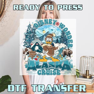 May include: White t-shirt featuring a colorful graphic of Donald Duck in winter attire, with the text "Disney Wonder Alaska Cruise." The design includes a bear, mountains, and an igloo. The words "Ready to Press" and "DTF Transfer" are also visible.