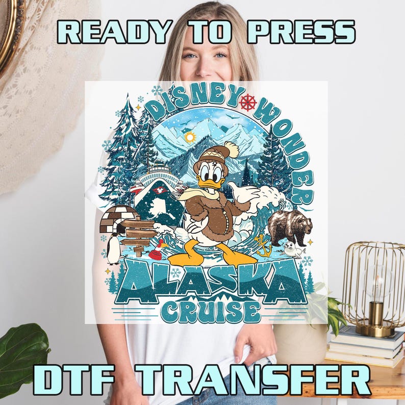 May include: White t-shirt featuring a colorful graphic of Donald Duck in winter attire, with the text "Disney Wonder Alaska Cruise." The design includes a bear, mountains, and an igloo. The words "Ready to Press" and "DTF Transfer" are also visible.