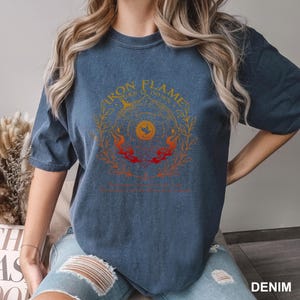 May include: A denim blue short-sleeve t-shirt featuring a graphic print in yellow, orange, and red. The design includes the text "IRON FLAME" and "TURN IT DOWN" surrounding a central circular emblem with a bird icon and flame motifs.