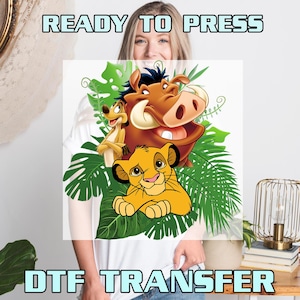 May include: White t-shirt with a ready to press DTF transfer featuring Simba, Pumbaa, and Timon from The Lion King. The transfer is surrounded by green tropical leaves.