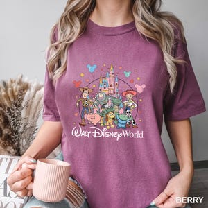May include: Berry-colored t-shirt featuring a graphic of Disney's Toy Story characters and a castle, with the text "Walt Disney World." The design includes Woody, Buzz Lightyear, and other characters. The word "BERRY" is printed at the bottom right.