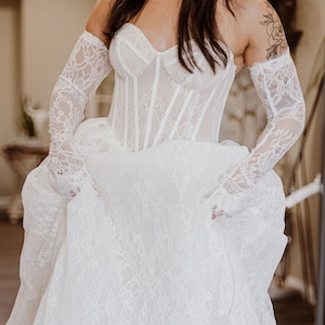 Ein Brautkleid mit aufwendigen Spitzendetails und einem Hauch Dramatik. Fotos zeigen unser aktuelles Kleid aus echten Fotoshooting, keine Katalogbilder.