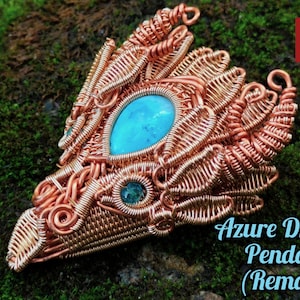 May include: A copper wire wrapped pendant in the shape of a dragon's head with a turquoise gemstone in the centre. The pendant is on a green mossy surface. The text "Azure Dragon Pendant (Remake)" is below the pendant.