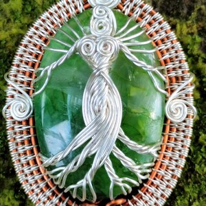 May include: A green gemstone pendant with a silver wire tree of life design, set in a copper wire frame.