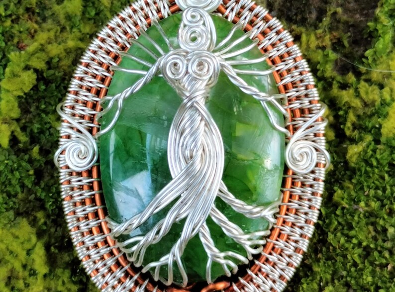 May include: A green gemstone pendant with a silver wire tree of life design, set in a copper wire frame.