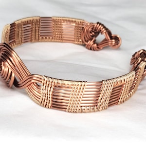 May include: A copper wire cuff bracelet featuring intricate woven patterns and coiled wire accents at both ends. The design consists of multiple strands of metallic copper wire meticulously wrapped and twisted to form a continuous, textured band.