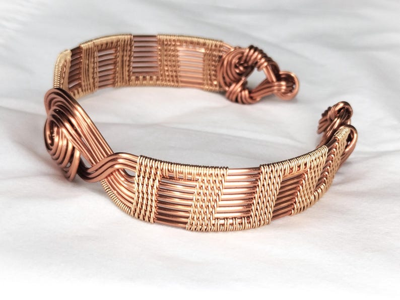 May include: A copper wire cuff bracelet featuring intricate woven patterns and coiled wire accents at both ends. The design consists of multiple strands of metallic copper wire meticulously wrapped and twisted to form a continuous, textured band.