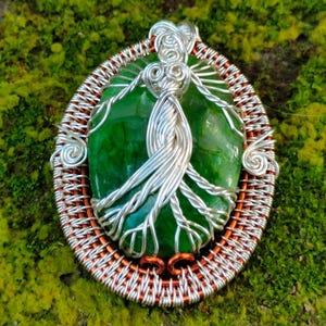 May include: A silver wire wrapped tree of life pendant with a green agate stone. The pendant is set in a copper wire frame.