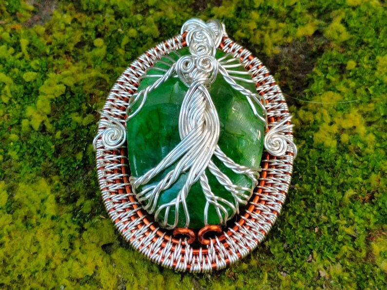 May include: A silver wire wrapped tree of life pendant with a green agate stone. The pendant is set in a copper wire frame.