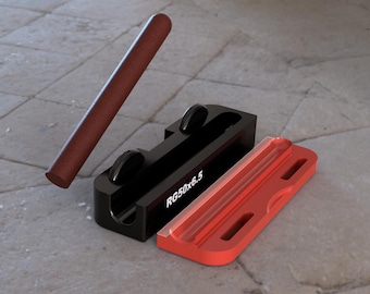 Op de afbeelding: Een zwart en rood gereedschap met een rood schuifstuk en een zwarte basis. De basis heeft twee zwarte wielen en de tekst "RG50x6.5" erop gedrukt. Een bruin cilindrisch voorwerp ligt naast het gereedschap.