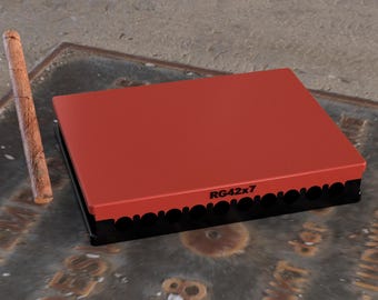May include: A rectangular red box with the text "RG42x7" on the side. The box has a black base with a decorative edge. A wooden dowel is next to the box.