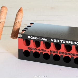 May include: A black and red storage box with the text "RG60-4.5in - NUB TORPEDO" and "RG60-4.5in - NUB ROUNDED" printed on the front. The box has multiple round holes and is designed to hold small objects. Two wooden dowels are shown next to the box.